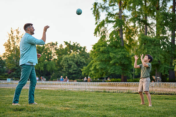Father and son playing catch in a vibrant park on a sunny summer afternoon, sharing joyful moments and strengthening their bond through active family fun and leisure