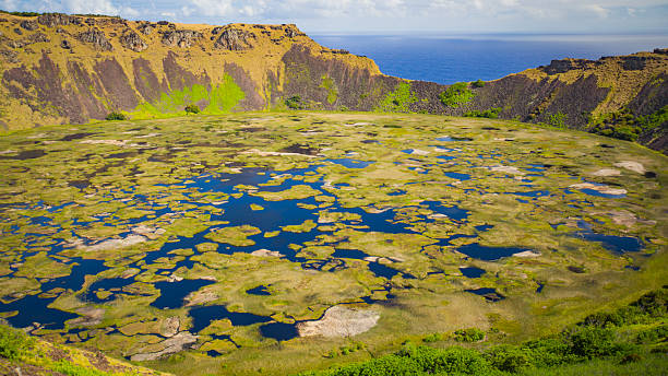 Dawn breaks over the tiny island of Easter Island in the South Pacific. This is the view looking across a pool towards Rano Raraku, an extinct volcano that became the quarry/birthplace of the iconic Moai statues that symbolise this magical landscape. The Moai were constructed around five or six hundred years ago and represent the islanders' ancestors. They were all toppled after a period of tribal warfare broke out, though a number were restored in the twentieth century.