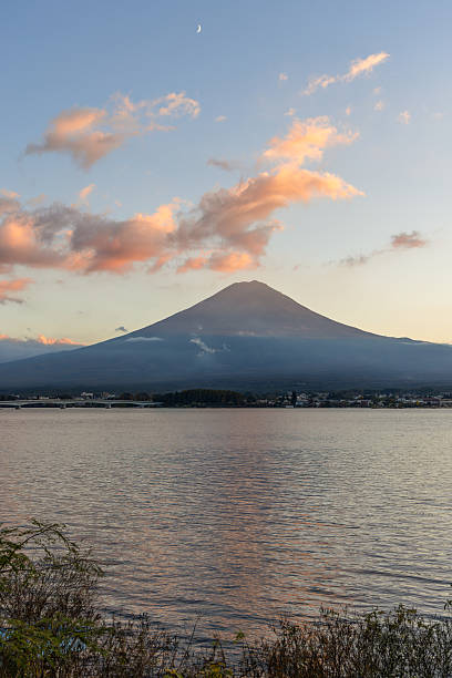 Golden hues of sunset highlight Mount Fuji slopes as scattered clouds float above, while Lake Kawaguchi shimmers with gentle ripples