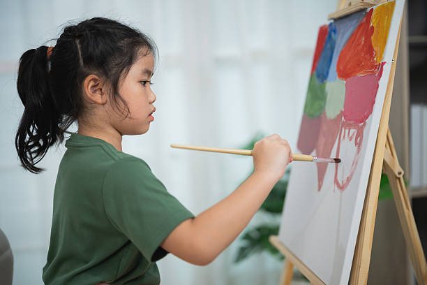 istock Young girl painting on canvas with bright colors indoors, focused on creative expression, artistic development and imagination in home setting 2219327140