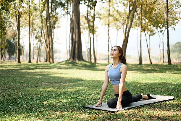 istock A young woman practices a deep yoga pose on a mat in a lush green park, surrounded by trees and sunlight in nature 2219328049
