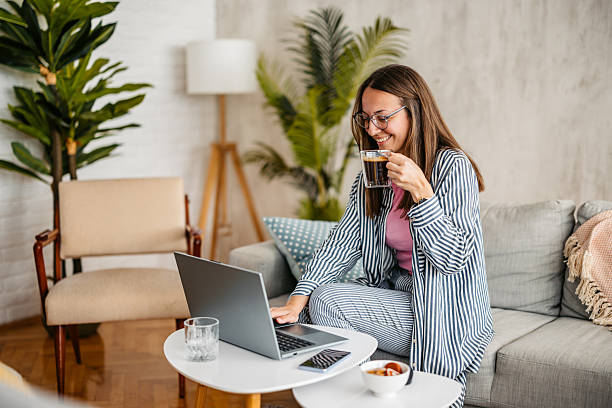 istock Young Woman Working On A Laptop And Drinking Coffee While Sitting On The Sofa At Home 2219329639
