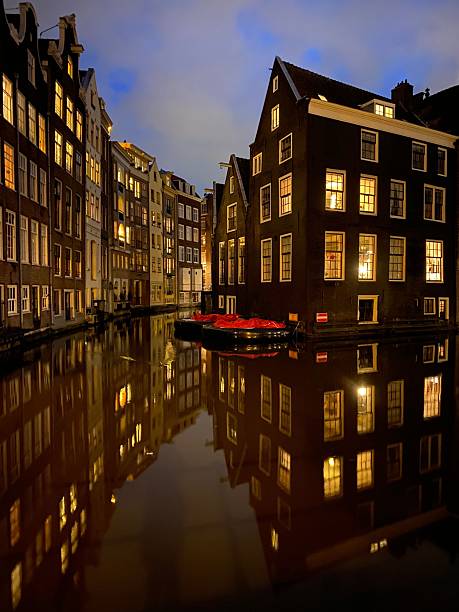 Night view of Amsterdam canal with illuminated historic buildings and reflections on water, showcasing Dutch architecture.
