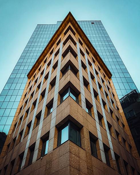 Low angle view of a modern office skyscraper, featuring sleek, reflective windows. The urban architecture is captured in an abstract, geometric, and minimalist style, highlighting the clean lines and contemporary design of the building.