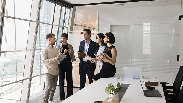 istock Five serious focused teammates gathered in skyscraper office meeting room 2219332037
