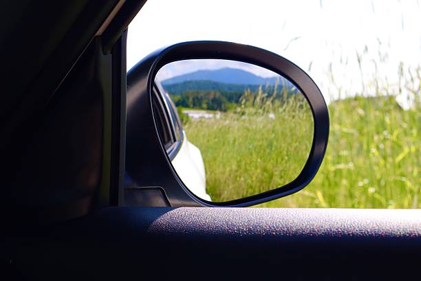 istock A side mirror reflects a green field and forested hills under a bright sky 2219332536