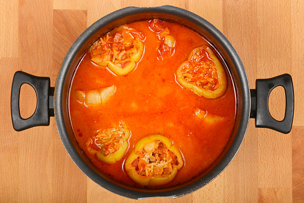 Overhead shot captures a pot of stuffed bell peppers in a rich, orange-red tomato sauce on a wooden background