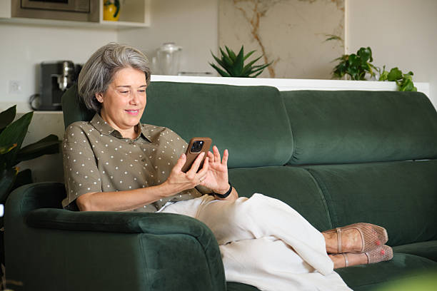 istock Smiling mature woman using smartphone relaxing on sofa at home 2219337582