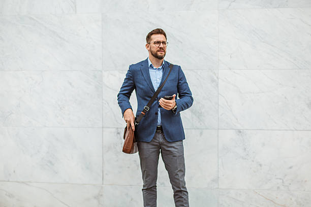 istock Businessman using smartphone holding leather bag in front of marble wall 2219339766