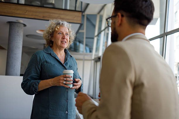 istock Professional businesswoman drinking takeaway coffee while conversing with coworker in corporate corridor 2219343588