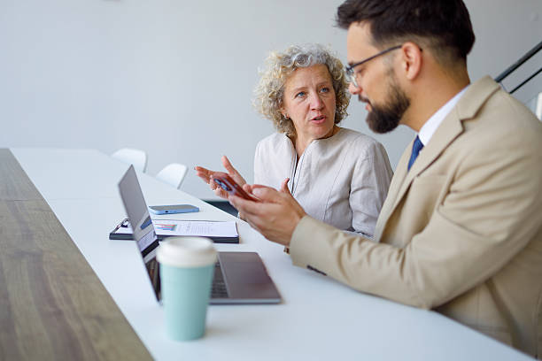 istock Two business people are discussing a project in a modern office, using a mobile phone and a laptop 2219345519
