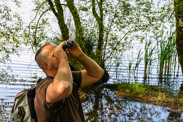 istock Strong man birdwatching with binoculars by a lake in natural environment 2219348598