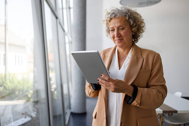 istock Smiling mature businesswoman using digital tablet while standing in modern office by the window 2219350090