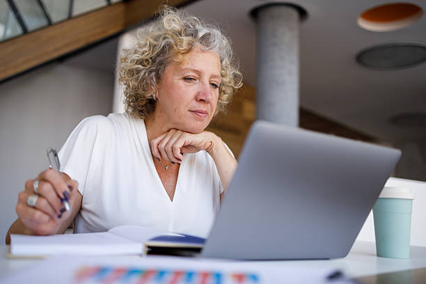 istock Professional female executive writing notes, working intently on laptop in contemporary workspace, wearing business attire 2219350824