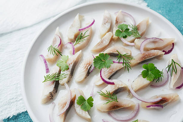 istock Marinated herring slices with red onion and herbs on white plate with napkin over blue background 2219353599