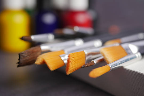Several paintbrushes lay on a canvas while vibrant paint bottles are visible.