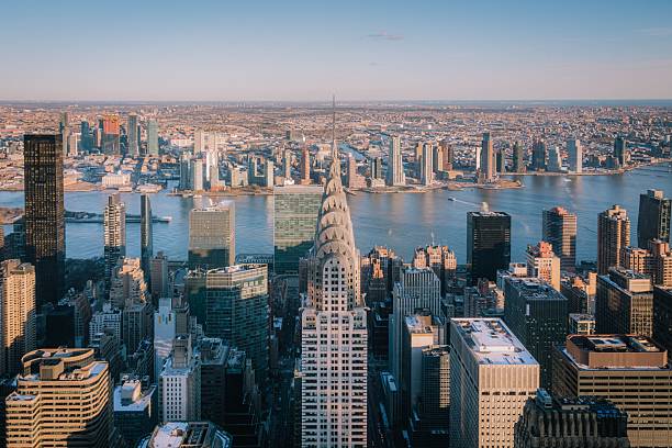 Aerial view of New York City skyline featuring the Chrysler Building and East River under a clear blue sky.