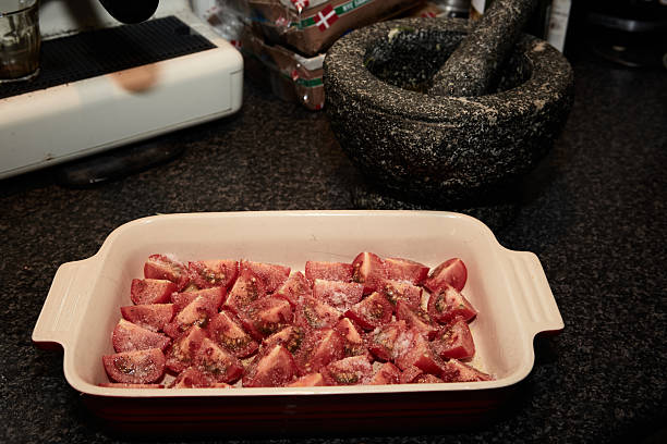Chopped cherry tomatoes in a baking dish seasoned with salt and sugar, ready to be baked in the oven