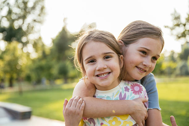 istock Two schoolage sister playing in the park, hugging and smiling at camera 2219358550