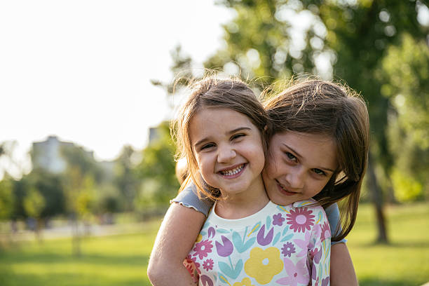 istock Two schoolage sister playing in the park, hgging and smiling at camera 2219358749