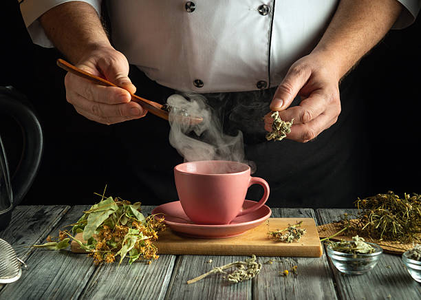 istock A person dressed in a chef's coat skillfully prepares herbal tea. Steam rises from a pink cup as dried herbs are added, showcasing the art of tea making 2219361377