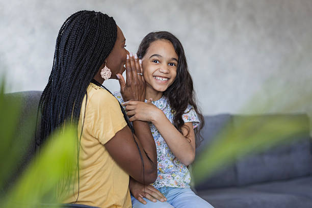 istock Woman whispering in her smiling daughter's ear 2219362165