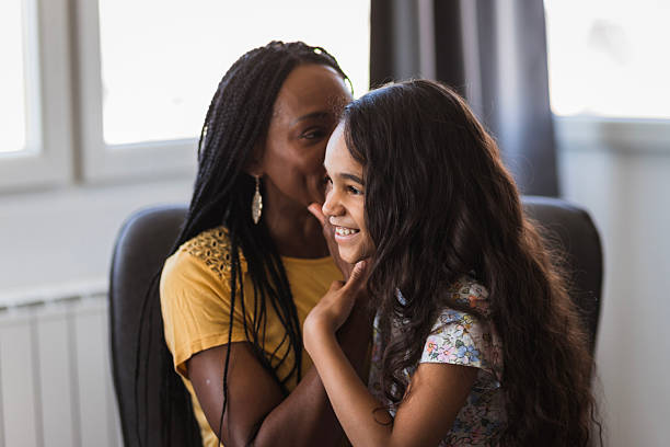 istock Woman whispering in her smiling daughter's ear 2219362245