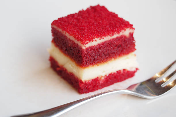 Stock photo showing close-up, elevated view of white, cake cutting board containing a whole, red velvet cake covered in butter cream and decorated with piped icing swirls dusted with dehydrated raspberry powder.