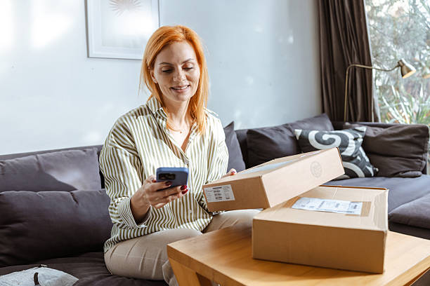 istock Woman unboxing a package while using her smartphone in a cozy living room 2219365572