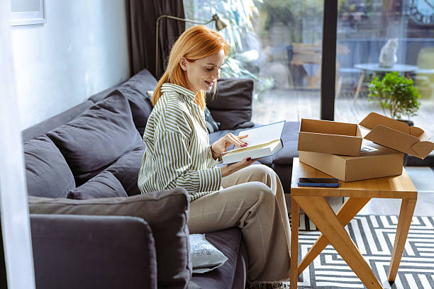 istock Woman unpacking parcel on sofa at home during a sunny day 2219365869