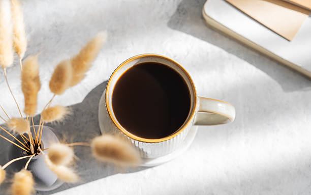 istock Freshly brewed espresso coffee in mug on a light table illuminated by the sun, with notebooks 2219368041