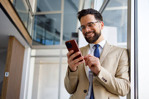 istock Businessman wearing suit and tie using smartphone in modern office building, smiling and looking at the screen 2219373747