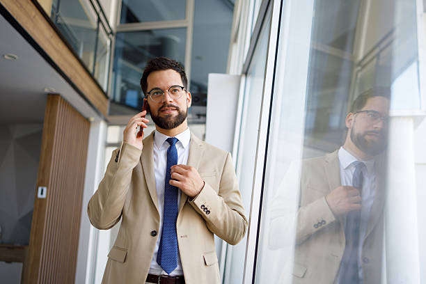 istock Professional businessman fixing tie during smartphone conversation in sleek corporate workspace 2219373825