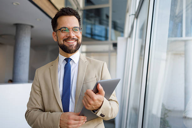 istock Smiling businessman using digital tablet while standing near window in contemporary workspace 2219374056