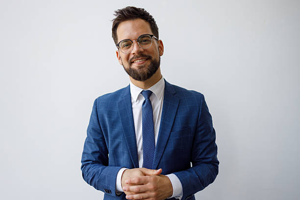 Portrait of a cheerful businessman wearing glasses and suit posing with his hands clasped on a white background