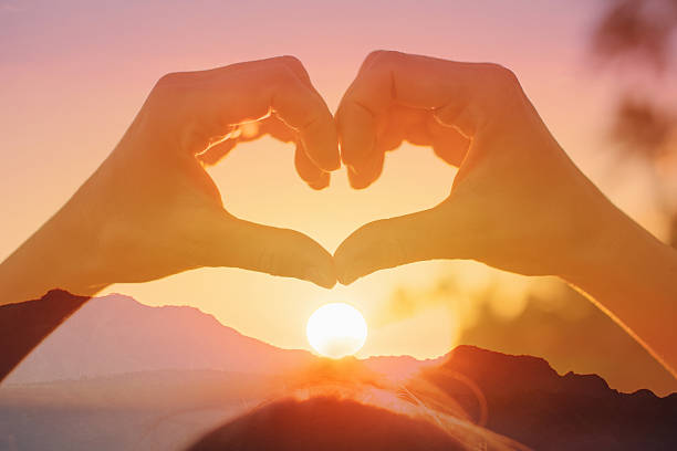 Hand making heart shape on beautiful sunset background.