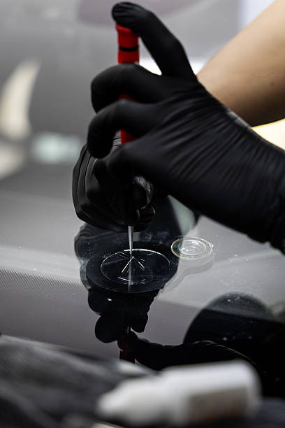 istock Awl is placed at the edge of a windshield crack for inspection or chip preparation. Technician uses a metal tool to apply controlled pressure on a glass chip. 2219389682