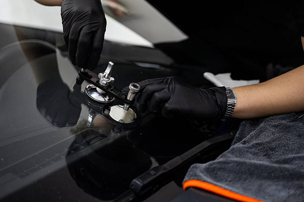 istock Technician uses a bridge tool to repair a car windshield crack with high-pressure resin injection. Windshield crack repair underway with a professional bridge tool and resin. 2219389709