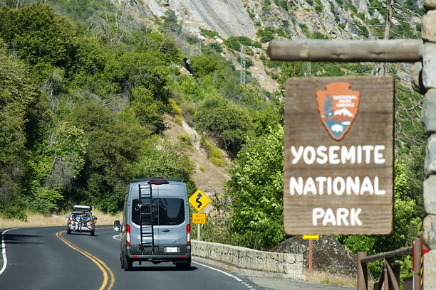 Mariposa County, California, USA - May 29, 2025: Vehicles enter Yosemite National Park at the El Portal entrance after passing by a wooden sign welcoming them to the popular destination in Northern California.