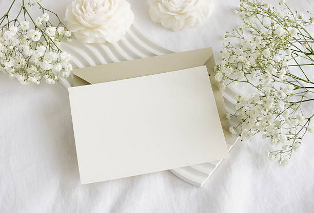istock Blank paper card mockup, envelope, white flowers and white table decor candles flowers on white linen textured background. 2219415520