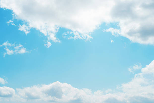 Beautiful sunny spring or summer sky background with copy space. Sun shining through the puffy clouds on blue sky