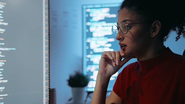 istock Gen Z Hispanic woman with glasses focused on coding on dual monitors working late at night 2219423532