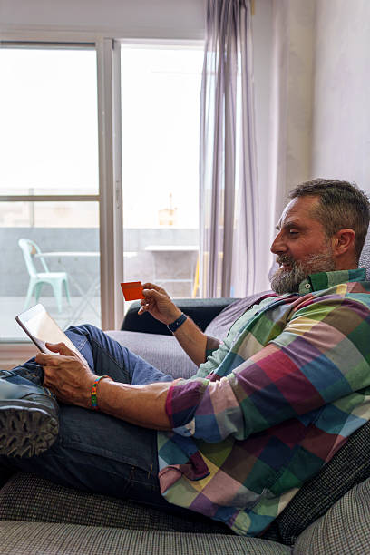 istock Mature man relaxing on sofa shopping online using digital tablet and credit card 2219426061