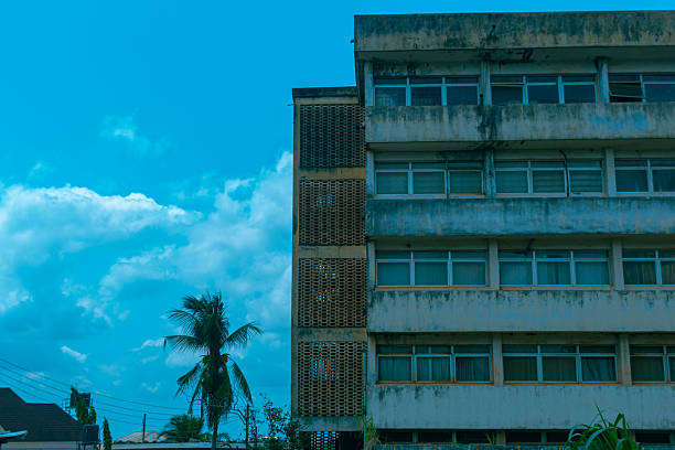 A weathered mid-century modern building with concrete sun breakers, palm trees, and a bright tropical sky in the background.