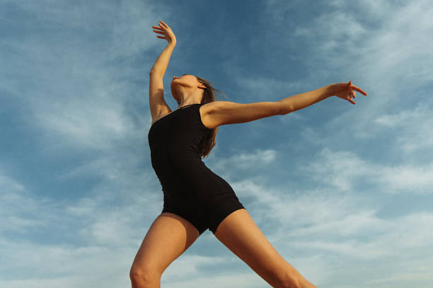 Woman gracefully dancing outdoors on a sunny day under a blue sky