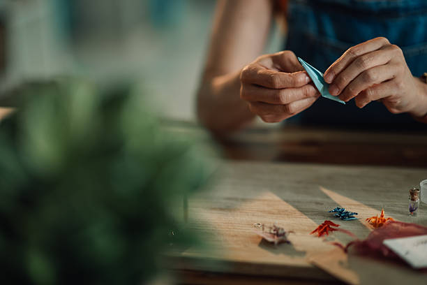 Woman carefully folding light blue origami paper creating small crane birds for jewelry making