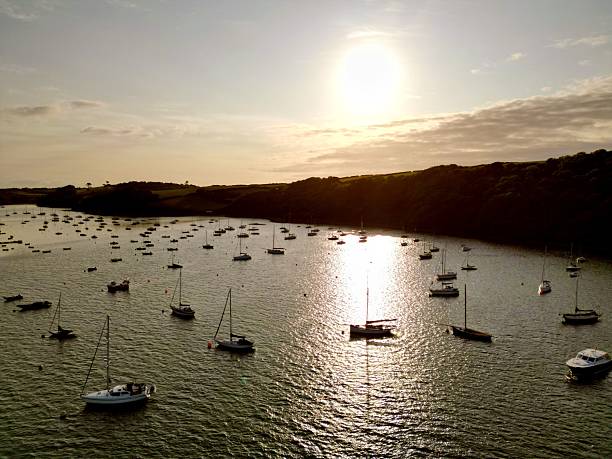 A scenic view of boats on a tranquil river at sunset, with a glowing sun reflecting on the water.