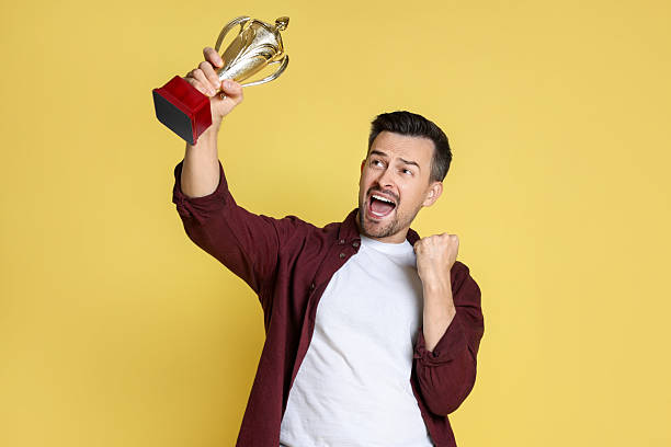 istock Happy winner with golden trophy cup on yellow background 2219433136