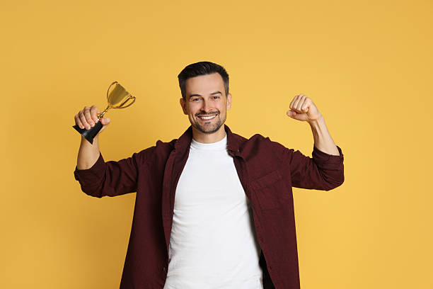 istock Happy winner with golden trophy cup on yellow background 2219433168