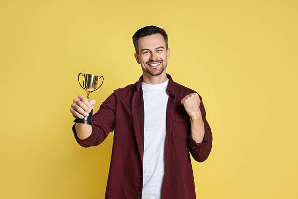istock Happy winner with golden trophy cup on yellow background 2219433176
